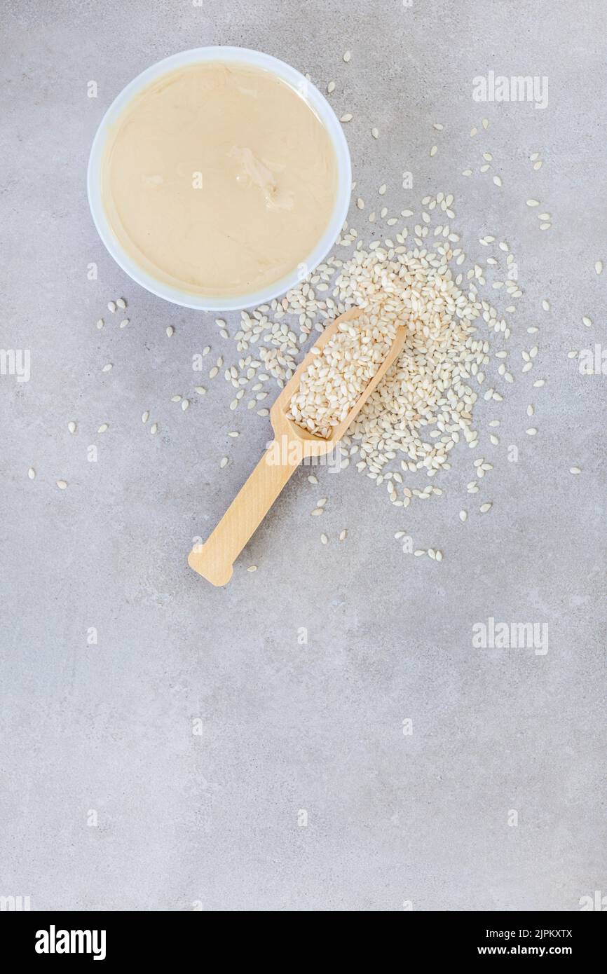 Pure sesame tahini with sesame seeds on mottled grey with copy space