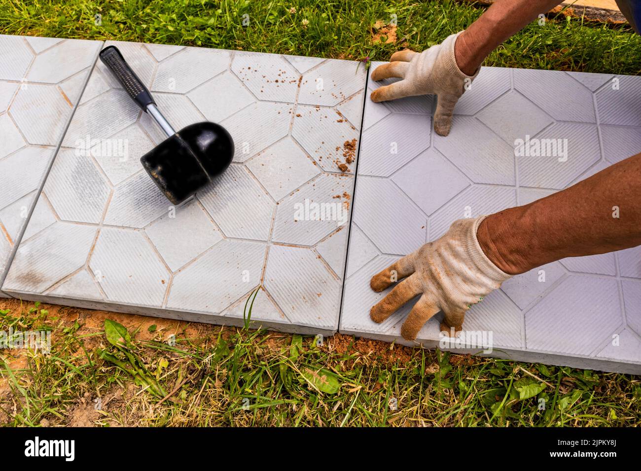 the hands of a worker in gloves lay tiles in a country house, cottage. Landscaping. laying of stone tiles Stock Photo