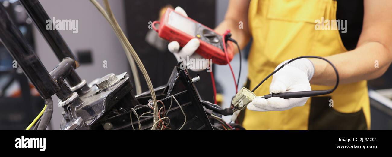 Mechanic using multimeter checks voltage level motorcycle battery motorcycle garage Stock Photo