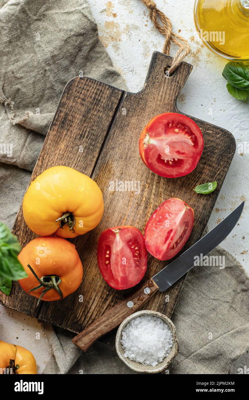Raw tomatoes and knife on wooden cutting board surrounded by ...