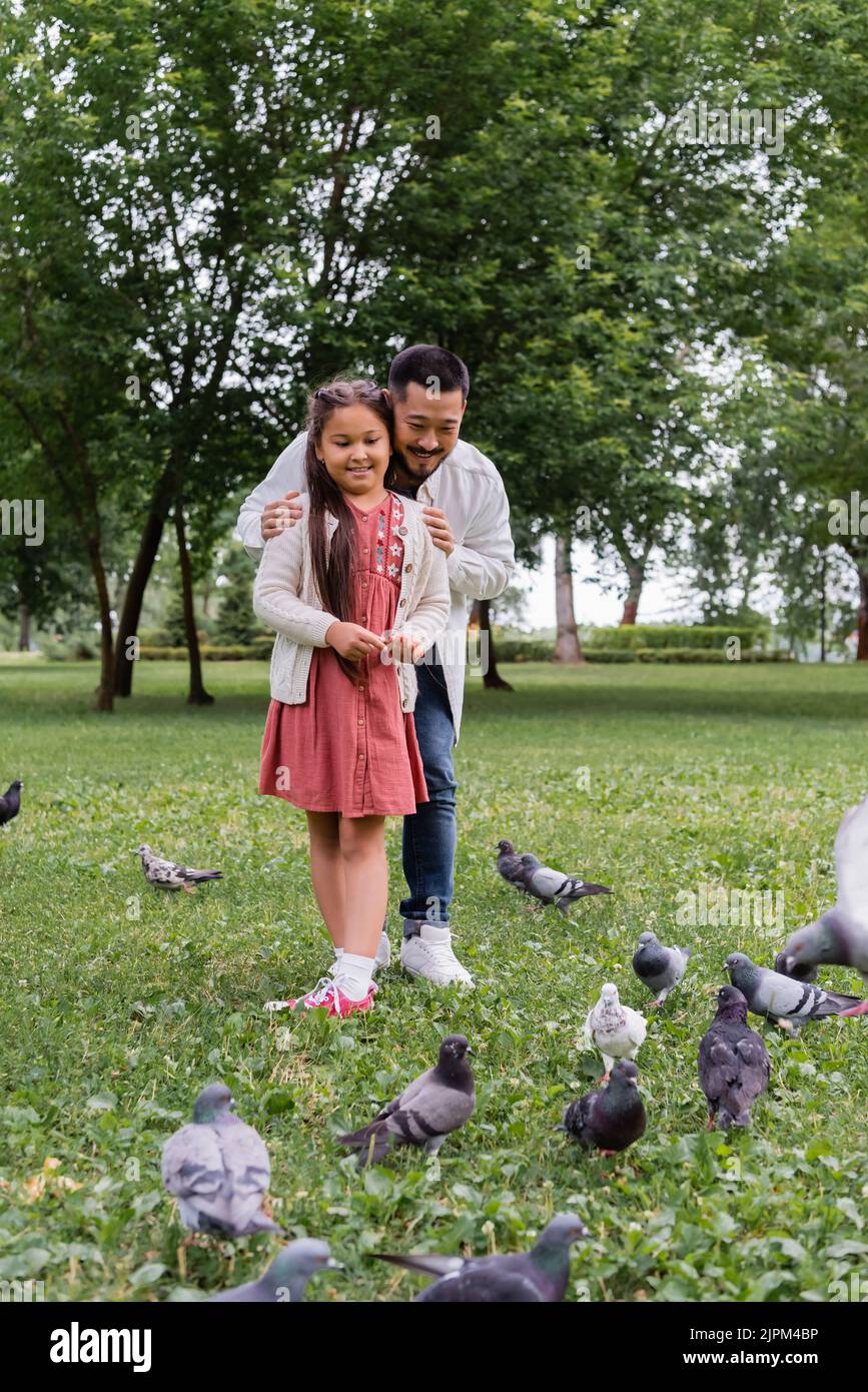 Asian parent hugging daughter near birds in summer park Stock Photo