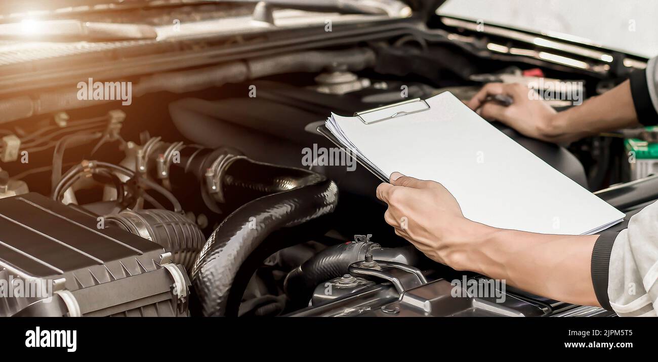 Automobile mechanic repairman checking a car engine with inspecting writing to the clipboard the checklist for repair machine, car service and mainten Stock Photo