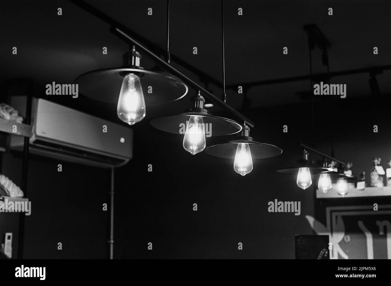 A grayscale shot of lamps on the ceiling in a cafe with lights on Stock Photo