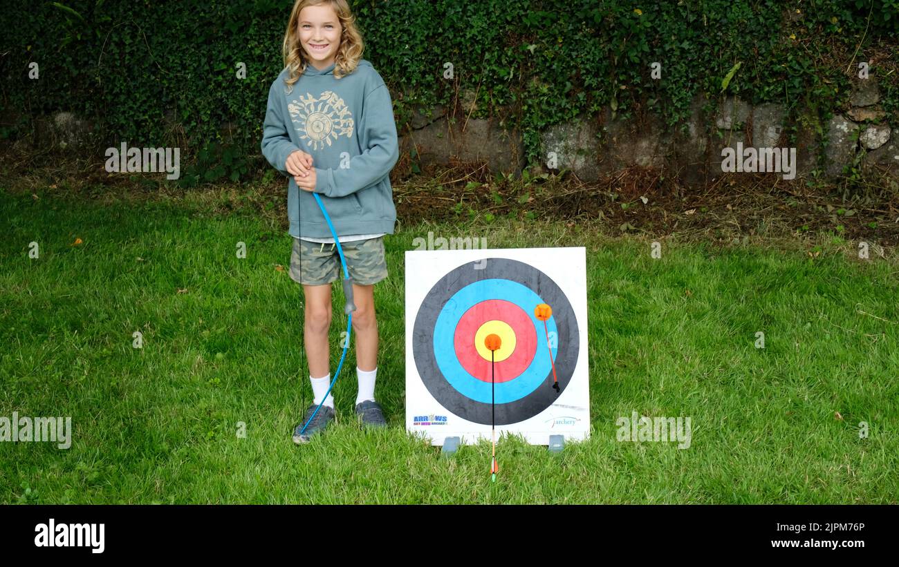 Young boy playing archery stands proudly by target after scoring a gold