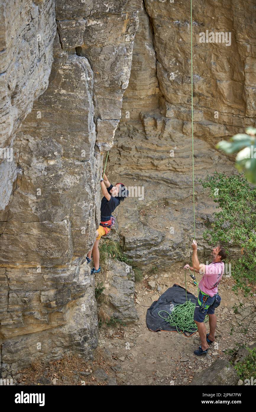 Teenage girl in a difficult rock climbing, secured by her dad in the ...