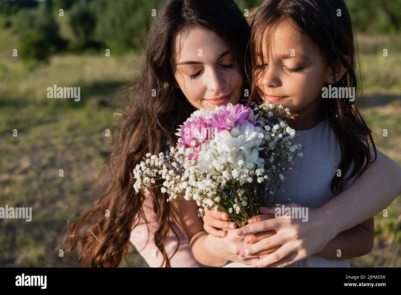 woman and girl with closed eyes smelling bouquet of aromatic flowers ...