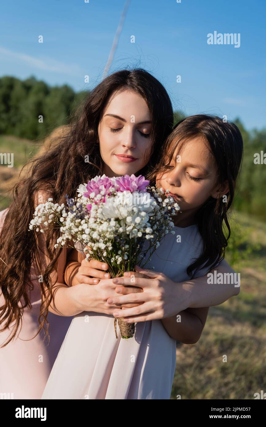 woman and child with closed eyes smelling aromatic flowers in blurred ...