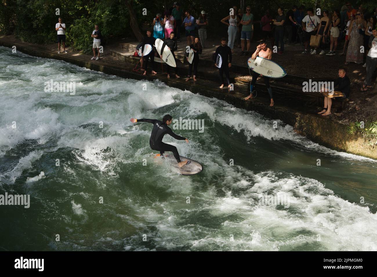 Surfer on the surfboard surfs on the artificial wave on the Eisbach River at the popular river surfing spot known as the Eisbachwelle (Eisbach Wave) in the Englischer Garten (English Garden) in Munich in Bavaria, Germany. Stock Photo