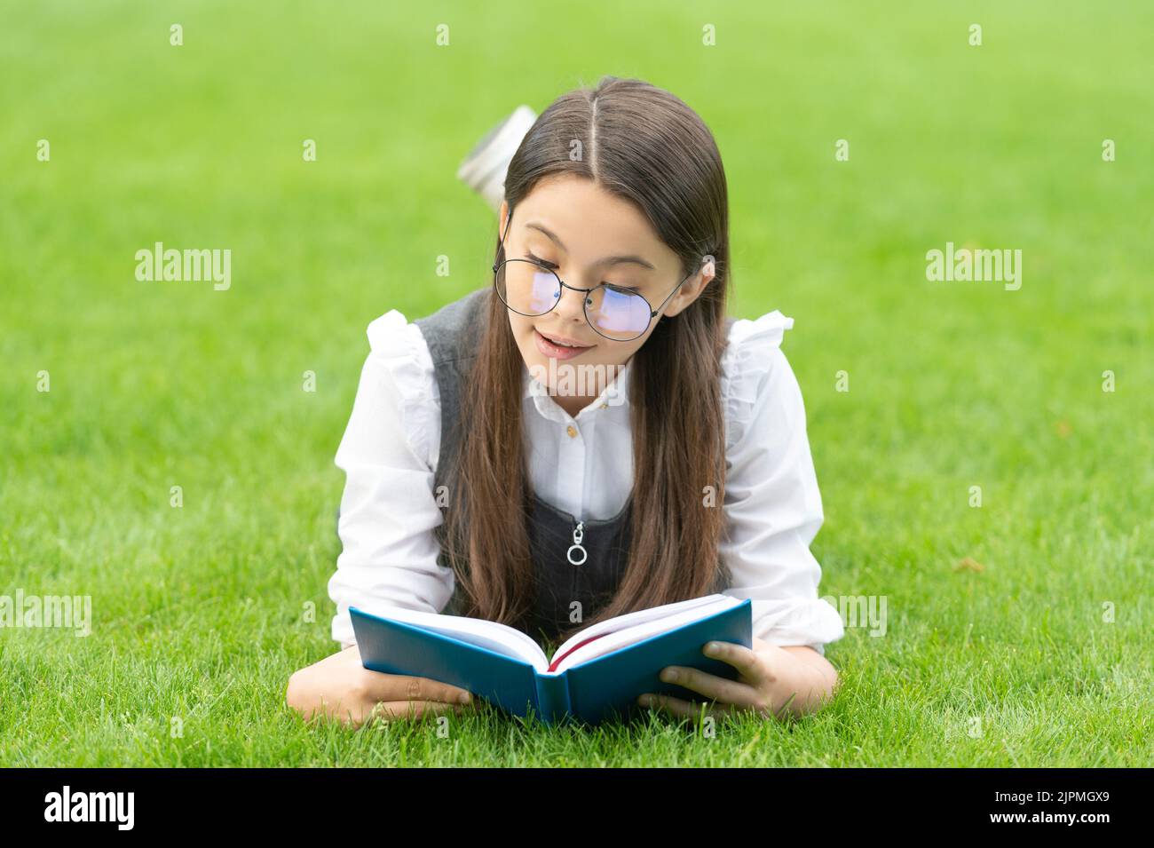 Reading Seriously Serious schoolgirl reading book lying on grass, reading. Teen girl ...