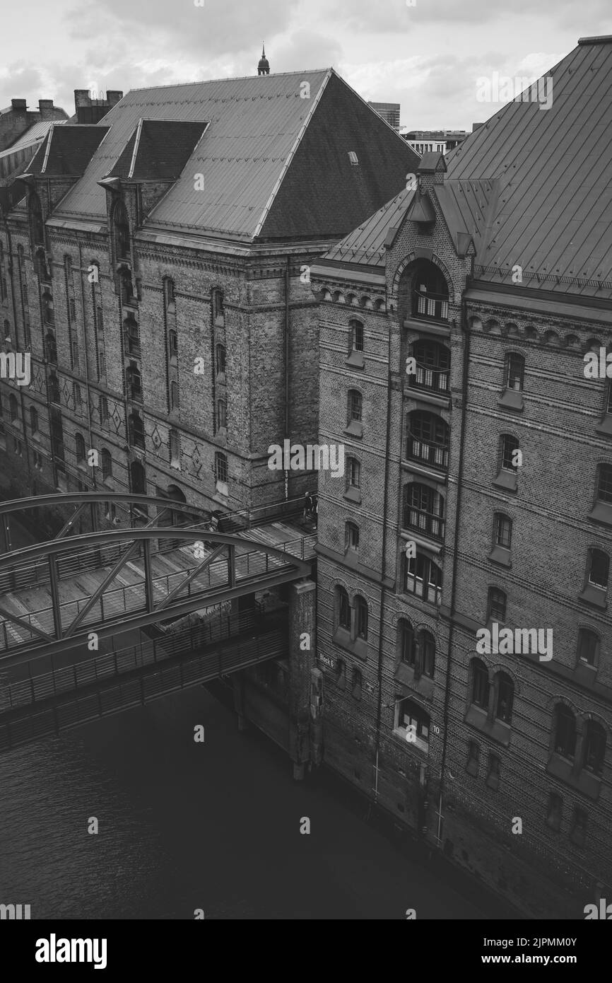 A grayscale vertical shot of the multi-storey buildings with entrances from water and land. Speicherstadt, Hamburg, Germany Stock Photo