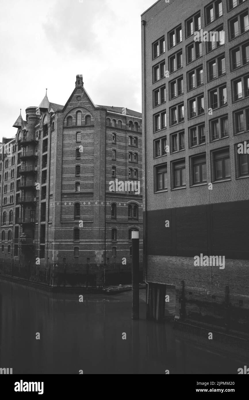 A grayscale vertical shot of the multi-storey buildings with entrances from water and land. Speicherstadt, Hamburg, Germany Stock Photo