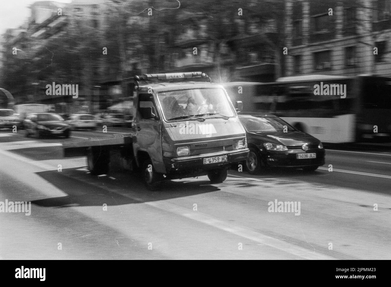 A grayscale shot of an old little truck and other vehicles on a city road Stock Photo