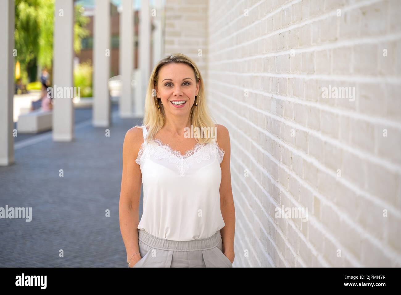 Relaxed friendly blond woman standing under a portico giving the camera a beaming smile Stock Photo