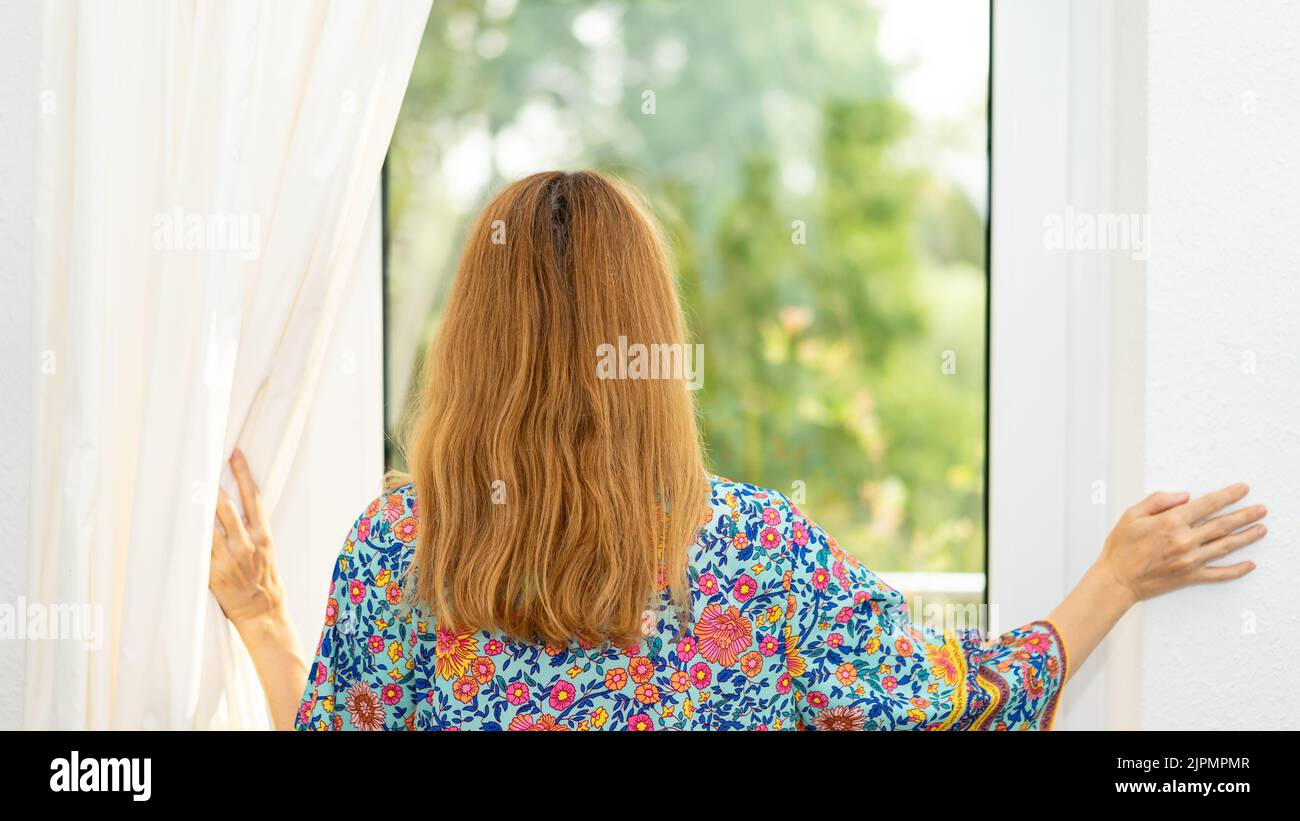 Young woman opens the window curtains in the morning Stock Photo