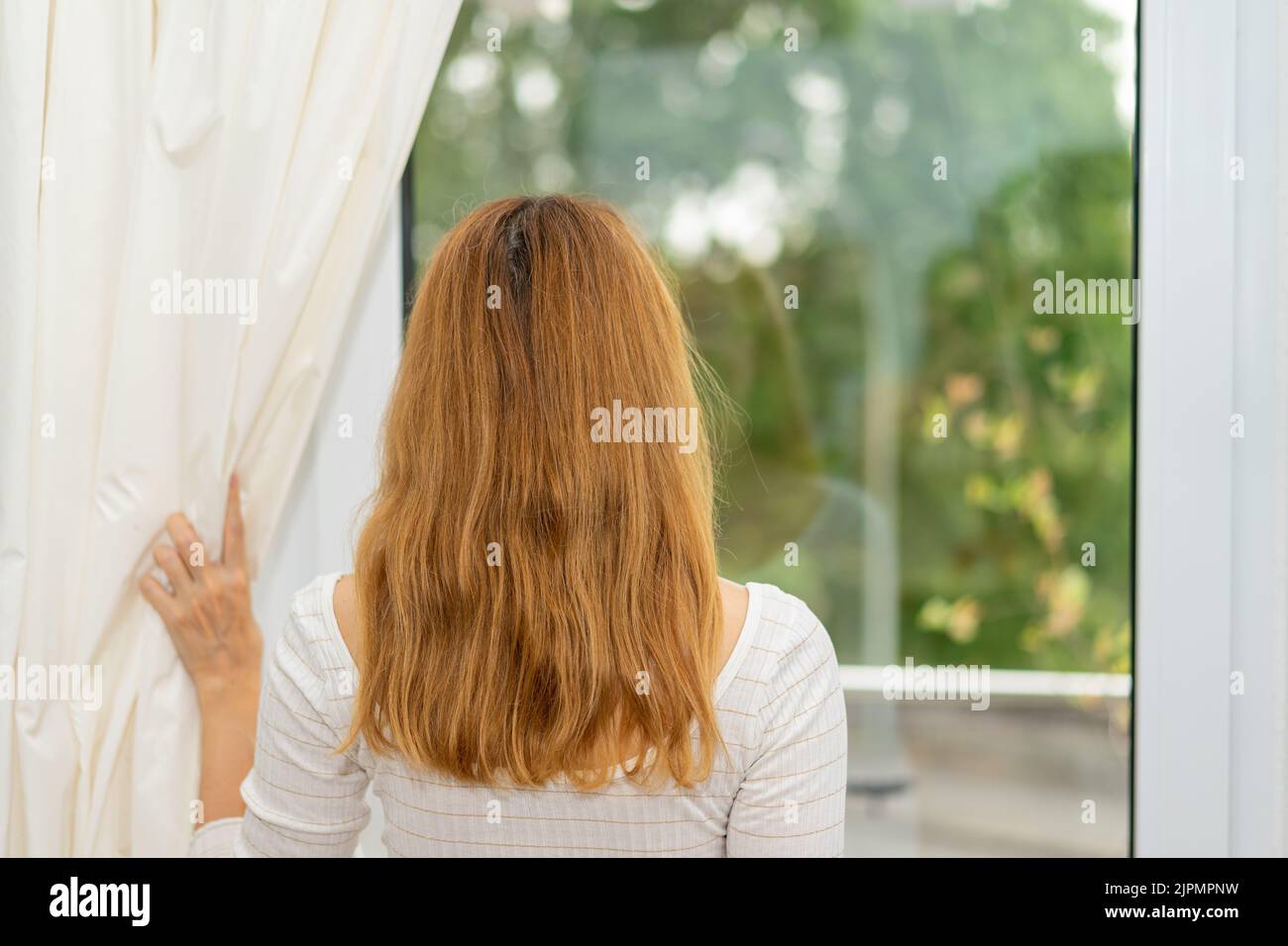 Young woman looks through the window, Stock Photo
