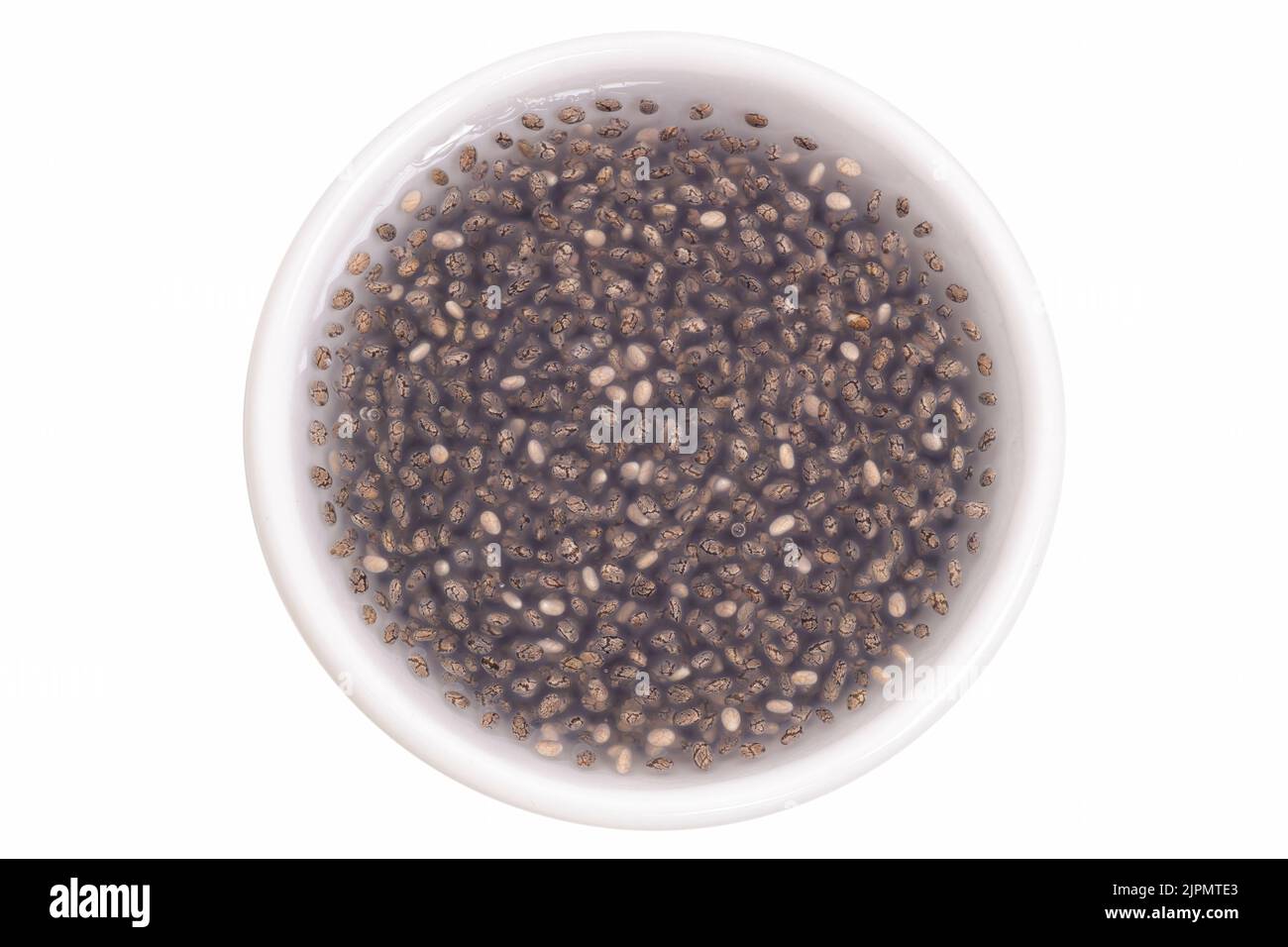Chia seeds soaked in water in a small white cup isolated on white, top view. Stock Photo