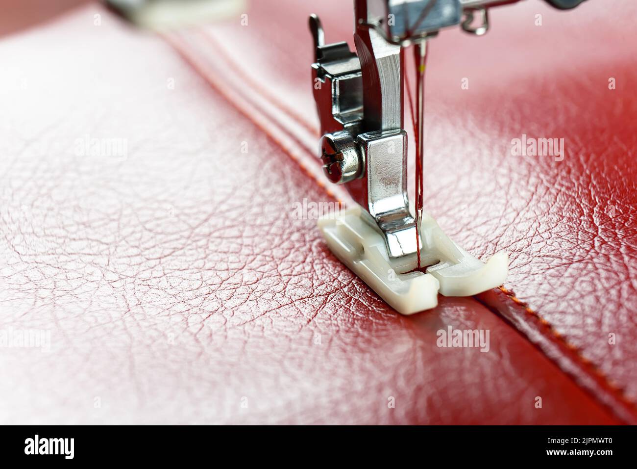 Modern sewing machine presser foot with a needle sews red leather