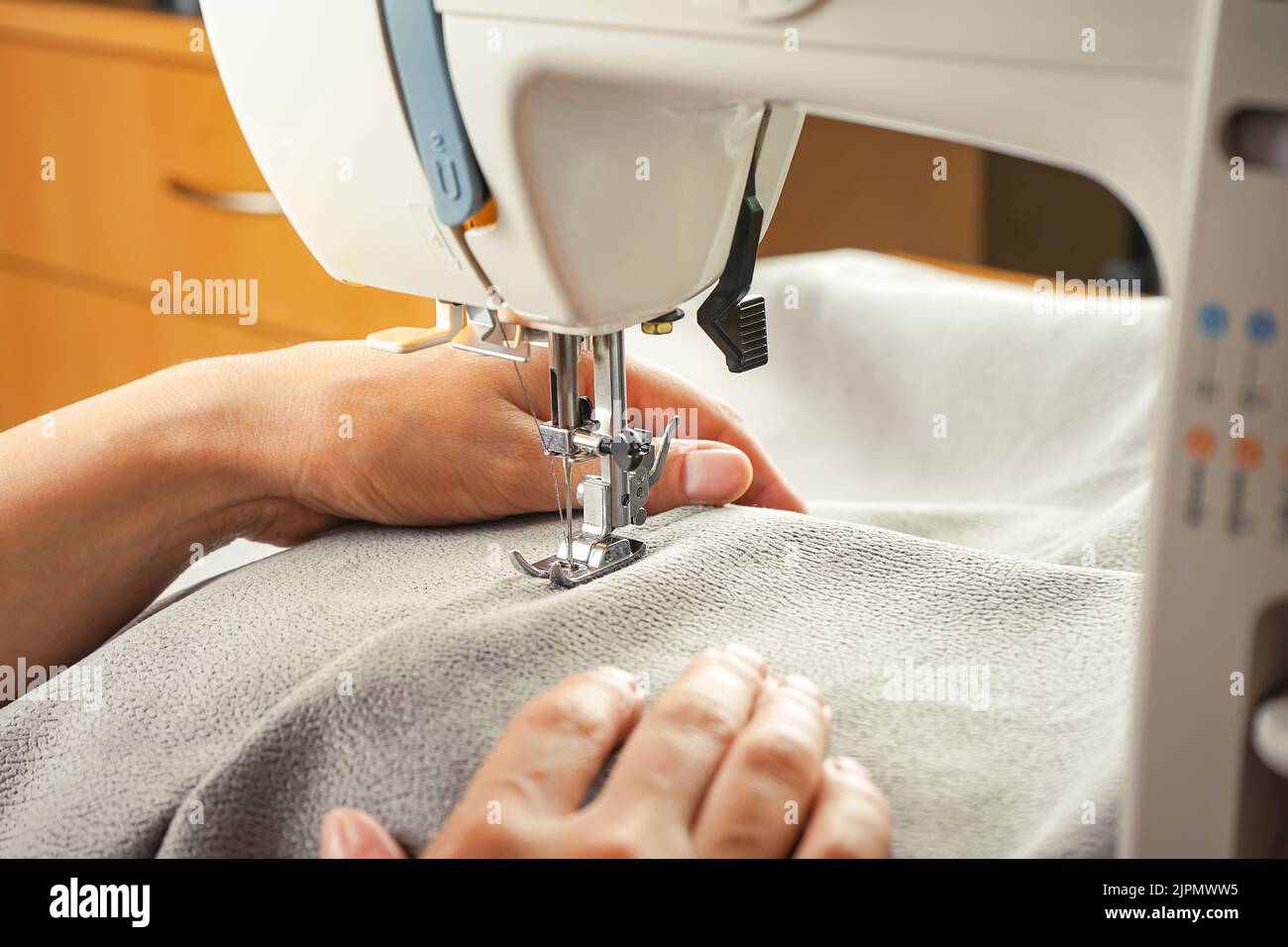 Seamstress female hands holding and stitching gray textile fabric on