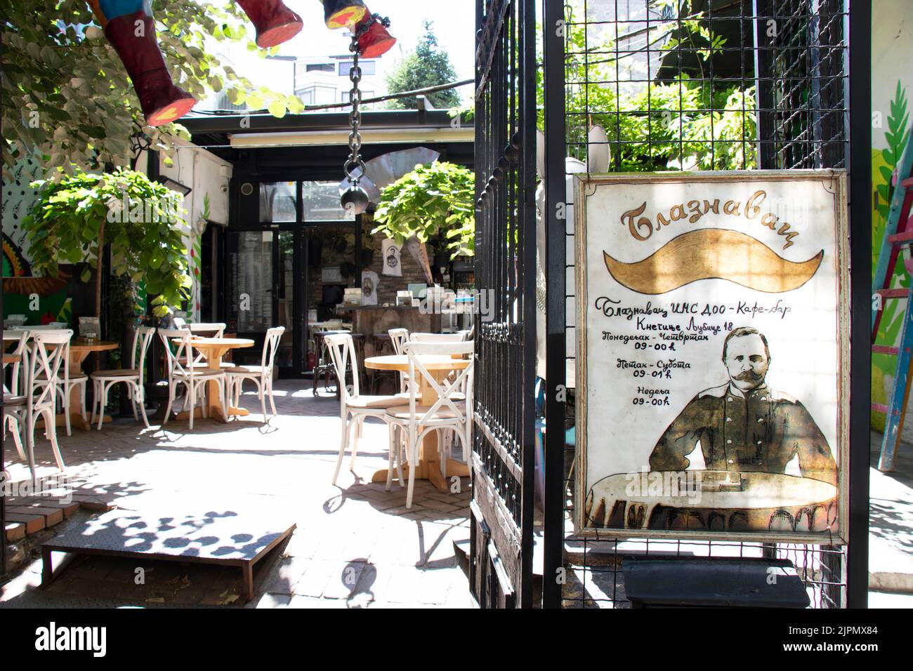 Belgrade-Serbia - June 15, 2022: Entrance to the garden of cafe-bar Blaznavac with outdoor sign board and chairs and tables inside a sunny garden Stock Photo