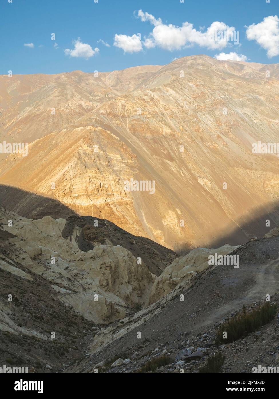 View across the Spiti valley with high ridges and steep slopes of Himalaya mountains under bright blue sky with clouds during summer near Kaza, India. Stock Photo