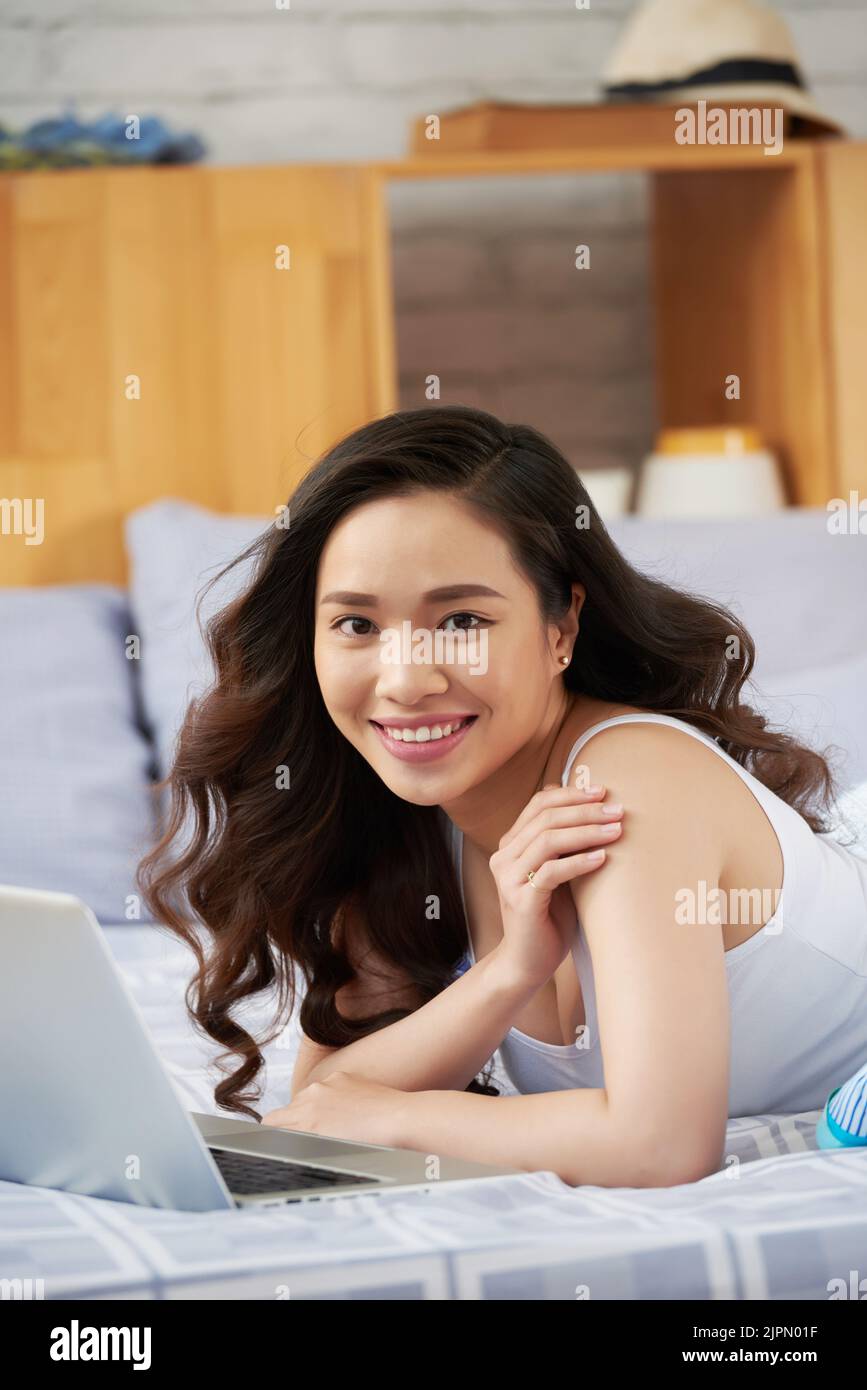 Portrait of attractive Vietnamese woman lying in her bed with laptop