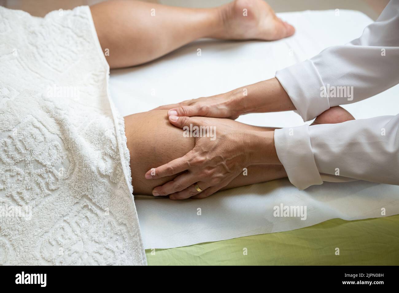 Goiânia, Goias, Brazil – July 18, 2022: A therapist dressed in white giving a leg massage to a patient lying on a stretcher. Stock Photo