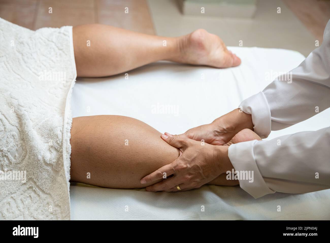 Goiânia, Goias, Brazil – July 18, 2022: A therapist dressed in white giving a leg massage to a patient lying on a stretcher. Stock Photo