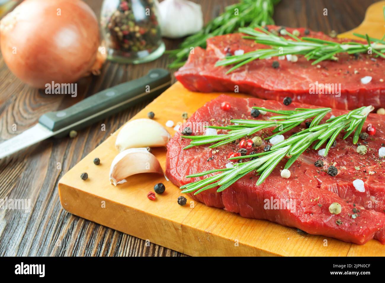 https://c8.alamy.com/comp/2JPN0CF/raw-beef-steak-with-vegetables-and-spices-on-cuting-board-and-brown-wooden-background-beef-steak-garlic-spice-rosemary-knife-2JPN0CF.jpg