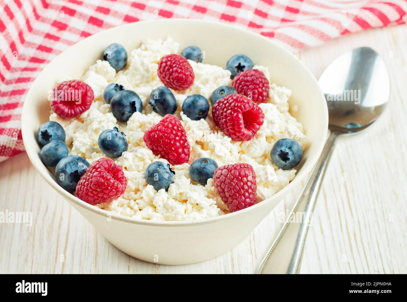 cottage cheese with raspberries and blueberries in a bowl on white wooden background. Dairy products, healthy food. Stock Photo