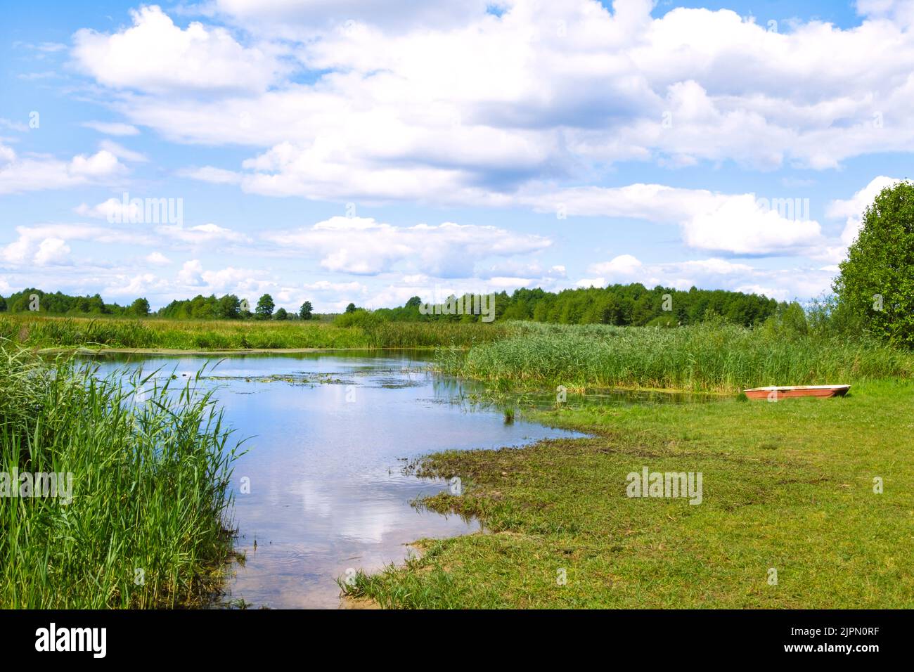 Idyll summer countryside landscape by the river. Boat by the bank, rushes and grass. Wild nature by Biebrza river with beautiful cloudscape reflect in Stock Photo