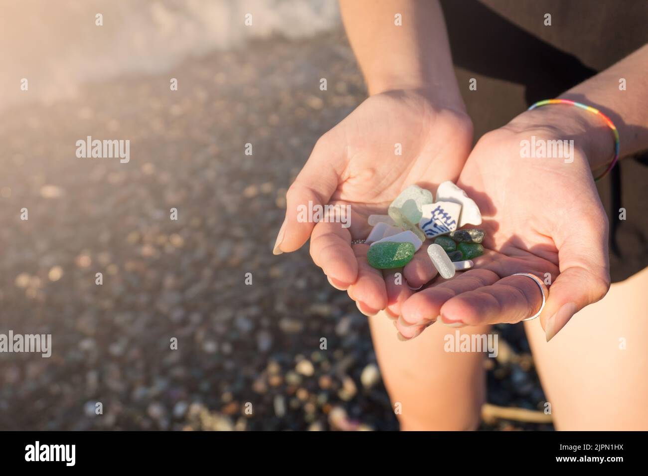 Sea glass and sea pottery pieces in the hands of a young woman with copy space. Stock Photo