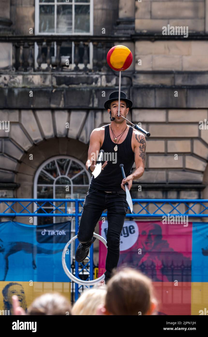 Edinburgh, Scotland, UK, 19th August 2022. Fringe performers on the Royal Mile: the street is packed with Fringe-goers and street performers on a sunny day. Pictured: Bob Glass, a juggler from New Zealand, in Parliament Square juggling with swords and spinning a ball. Credit: Sally Anderson/Alamy Live News Stock Photo