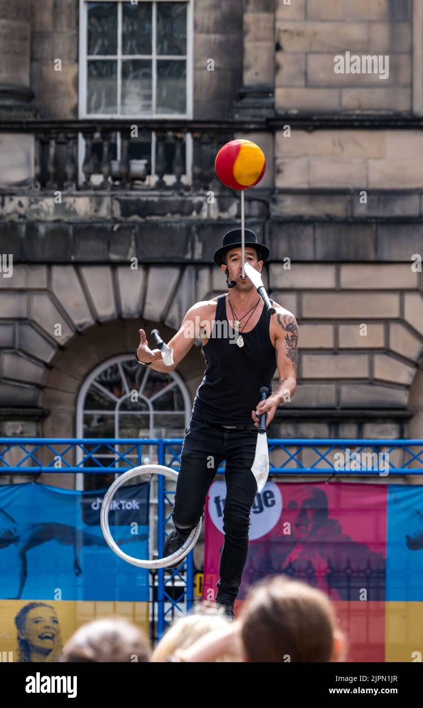 Edinburgh, Scotland, UK, 19th August 2022. Fringe performers on the Royal Mile: the street is packed with Fringe-goers and street performers on a sunny day. Pictured: Bob Glass, a juggler from New Zealand, in Parliament Square juggling with swords and spinning a ball. Credit: Sally Anderson/Alamy Live News Stock Photo