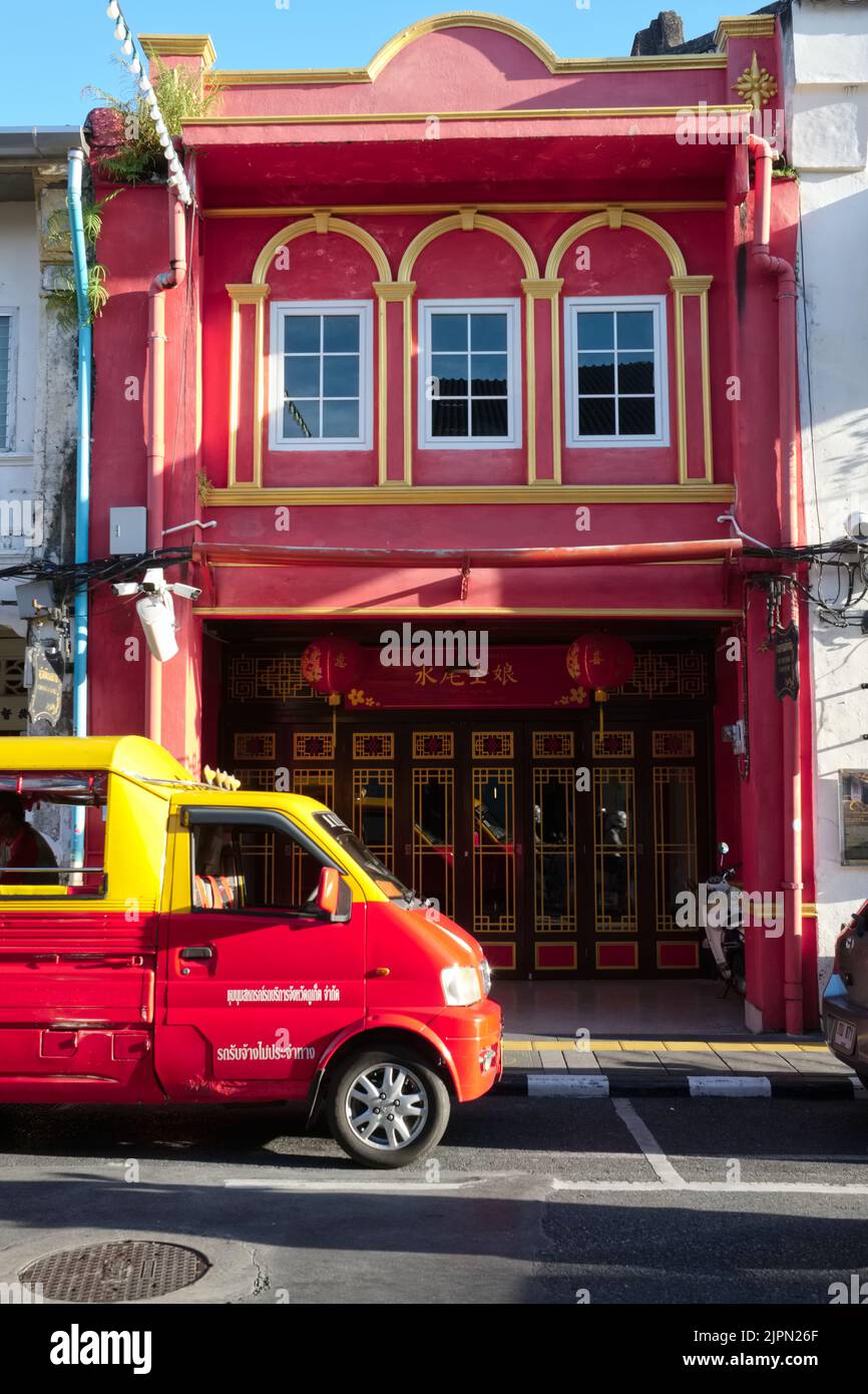 A red-and-yellow tuk-tuk (4-wheeler taxi) in front of a Sino-Portuguese or Perankan house in Thalang Rd in the Old Town area of Phuket Town, Thailand Stock Photo