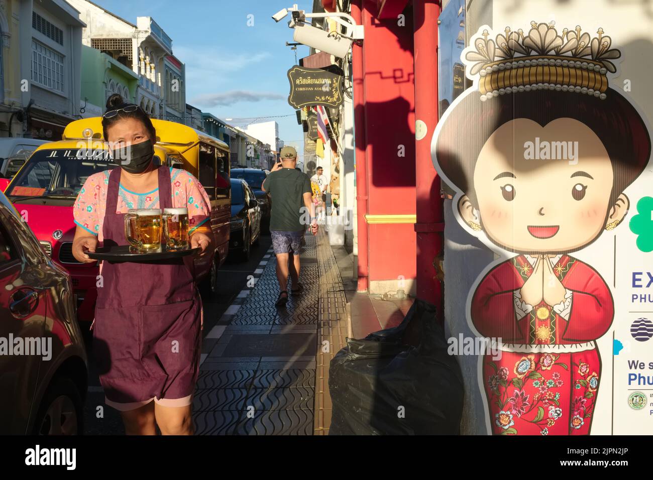 A waitress carrying a beer tray in Thalang Rd in the Old Town area of Phuket Town, Thailand, a street lined with restaurants, cafes, pubs & boutiques Stock Photo