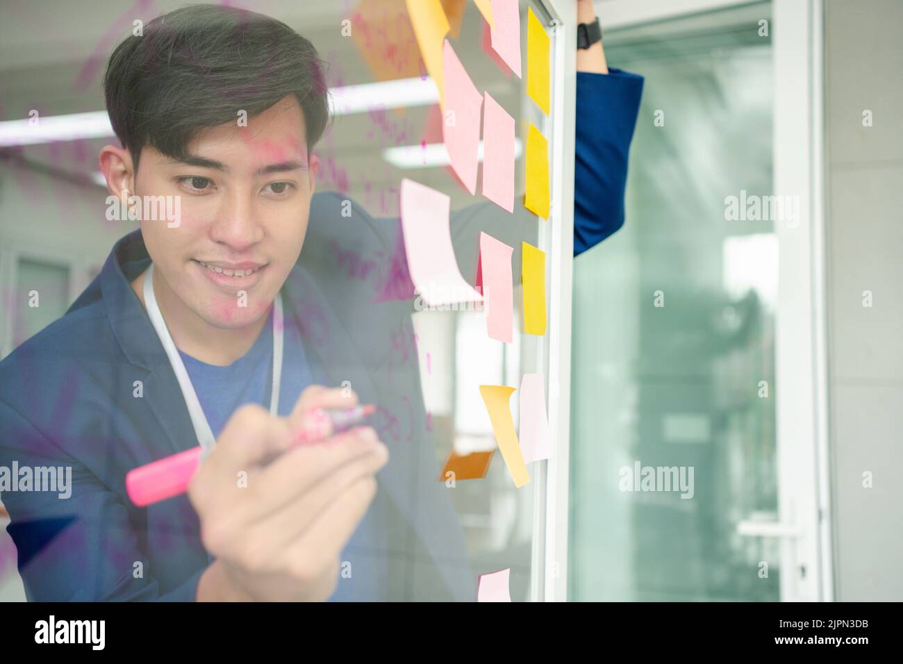 Young Creative businessman holding a marker and writing plan and share idea on glass wall with sticky note, Brainstorming and discussing and formulati Stock Photo