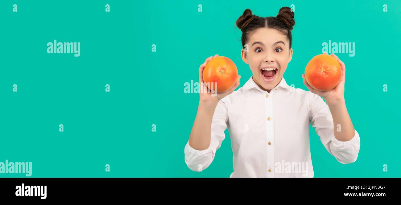 cheerful teen girl wear uniform holding grapefruit on blue background, vitamin. . Child girl portrait with pomelo grapefruit orange, horizontal poster Stock Photo