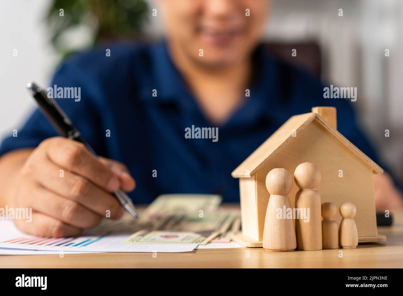 Selective focus for House model and figures people in front Happy Asian man holding a banknote and do financial accounting, Concept for financial plan Stock Photo