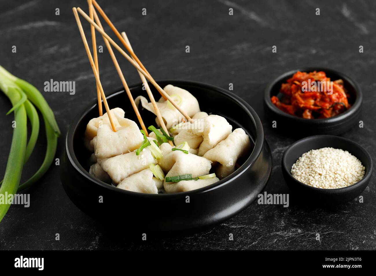 Korean Odeng Tangeomuk Odeng Guk, Korean Fish Cake Soup in Traditional Pot on Black Table Background. Served with Kimchi Stock Photo