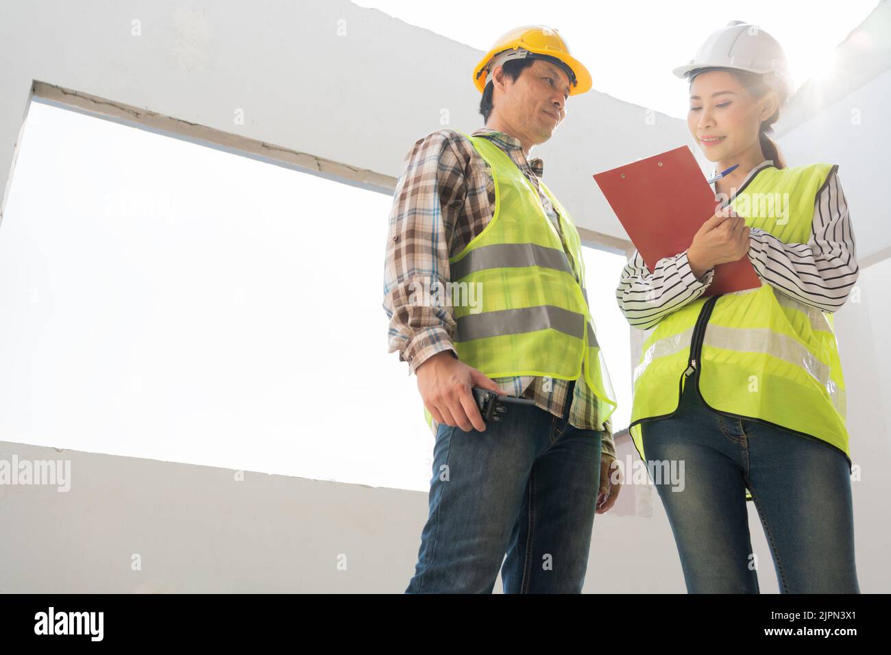 Asian engineer or Young Female Architect put on a helmet for safety and talk with a contractor on a construction building factory project, Concept of Stock Photo