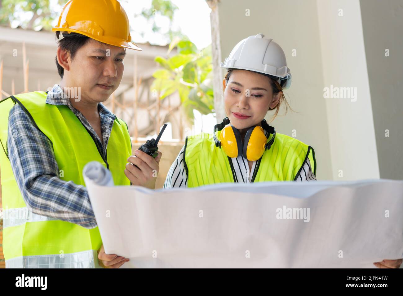Asian engineer or Young Female Architect put on a helmet for safety and talk with a contractor on a construction building factory project, Concept of Stock Photo
