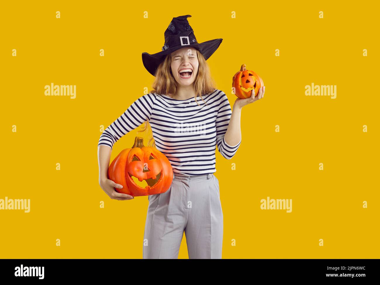 Portrait of a happy, funny woman in a witch hat holding Halloween pumpkins and laughing Stock Photo