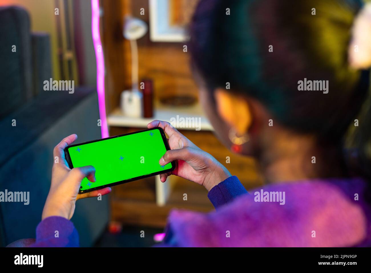 Shoulder shot of teenager girl playing video game on green screen mobile phone at home - concept of enteraiment, gaming addiction and technology Stock Photo