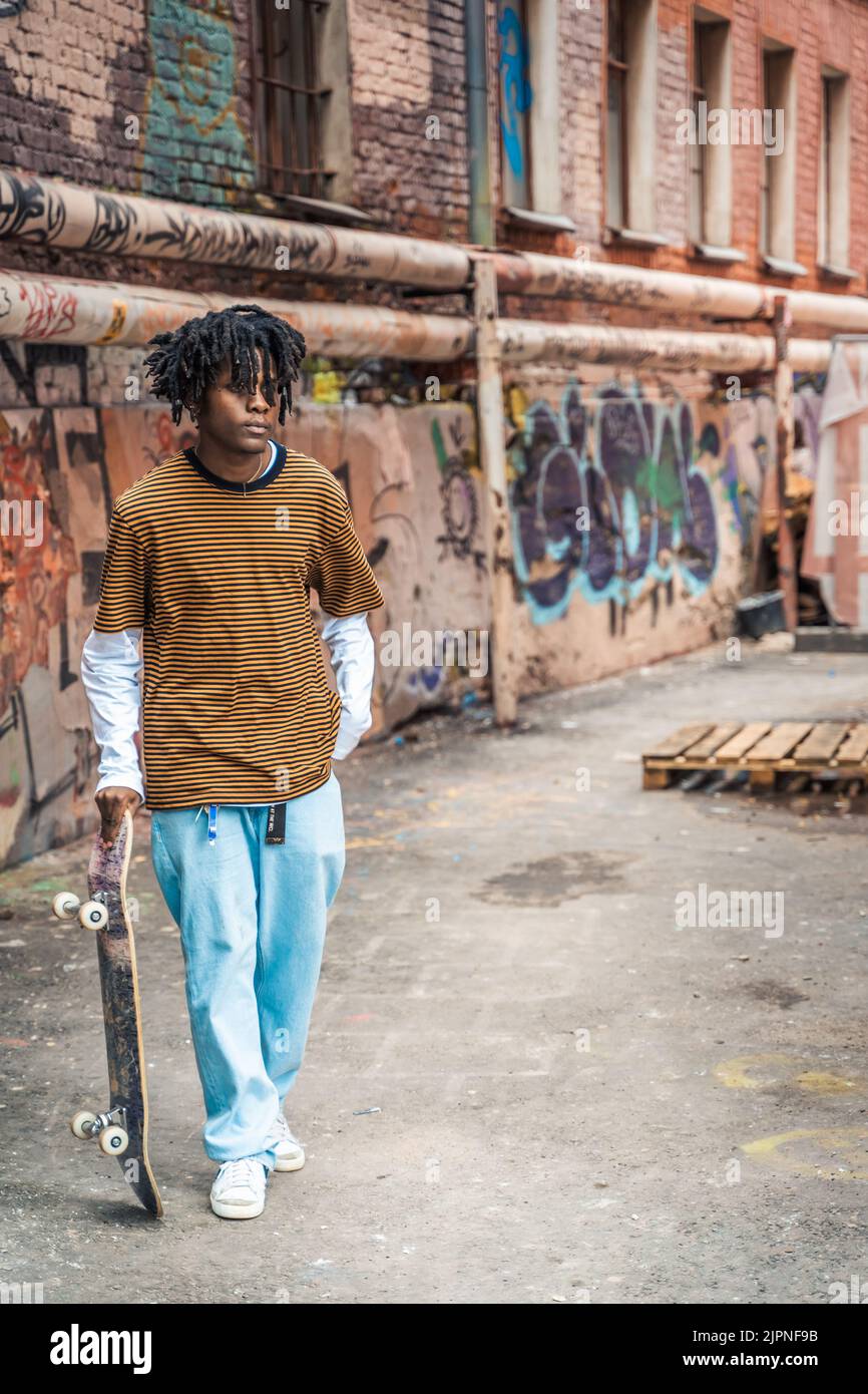 Young handsome stylish black man with natural hair dreadlocks. Afroamerican guy.Stairs,wall painted with graffiti in poor quarter of street art cultur Stock Photo