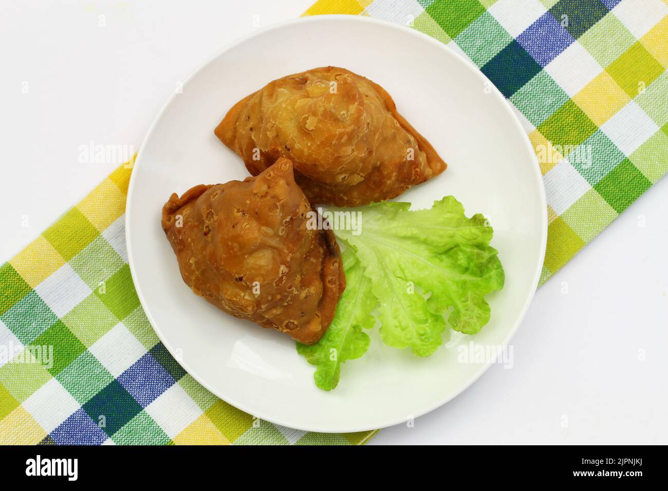 Two Indian samosas on green lettuce on white plate on checkered cloth Stock Photo