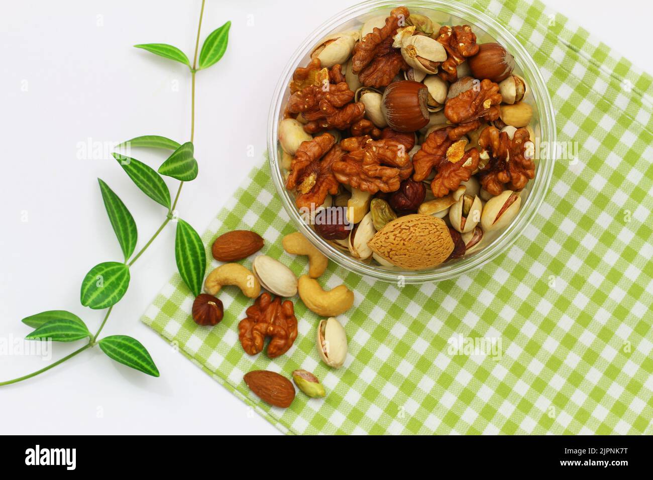 Pistachios, walnuts, cashew nuts, hazelnuts, peanuts, almonds in bowl on green and white checkered cloth Stock Photo