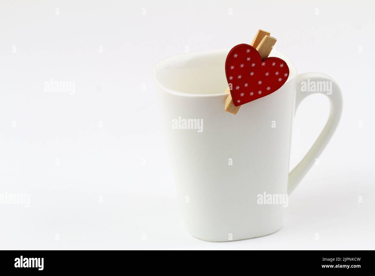 Wooden clip with dotted red heart on top of white coffee mug with copy space Stock Photo