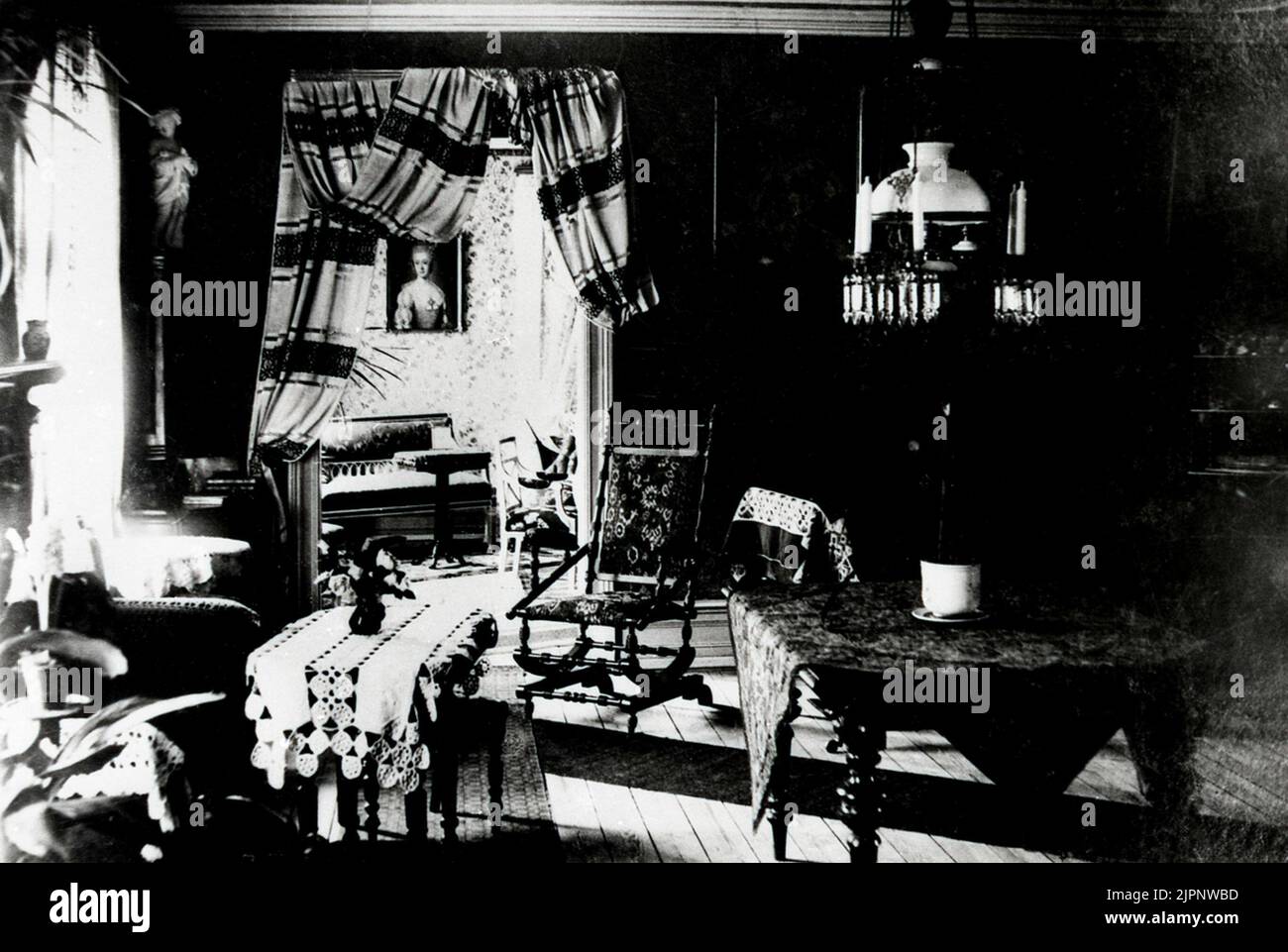 The Storgatan 20 property was acquired in 1900 by company N. Ekman. Otto & Helga Warenberg's home, Storgatan 20. German plot. Photo taken 1902 before the auction. The camera has been standing in front of the tambourine door. You look through the 'hall' into the atrium. The queen board hangs on the outer wall towards Ekman's alley. The windows are towards Storgatan. The wide white embroidery at the rocking chair belongs to a large cloth, which covers the table piano, which in its time was passed on the road to Höryda, Härlunda, Helga's home. The curtains were home -woven. Fastigheten Storgatan Stock Photo