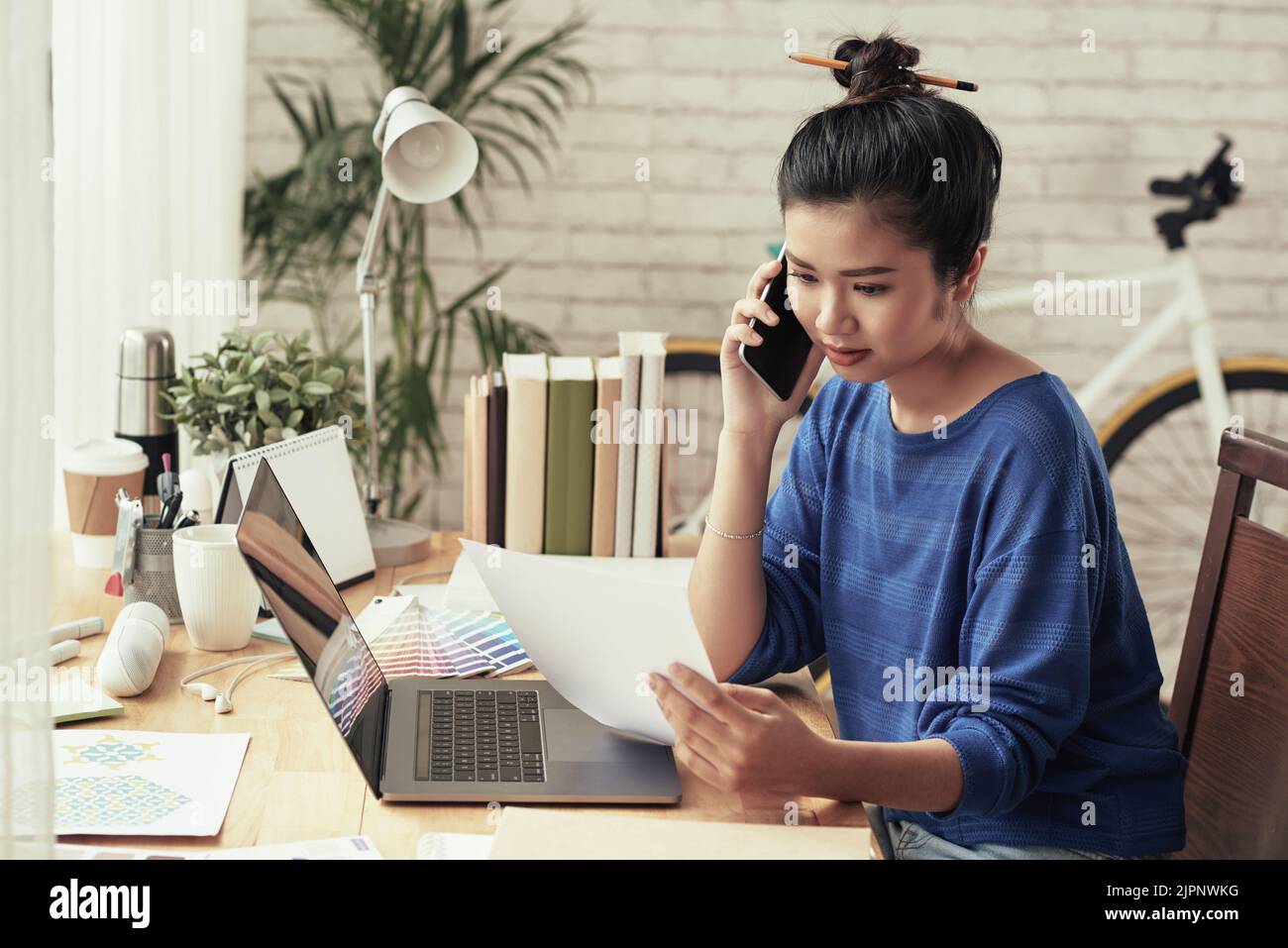 Young Vietnamese graphic designer reading document and calling to client Stock Photo