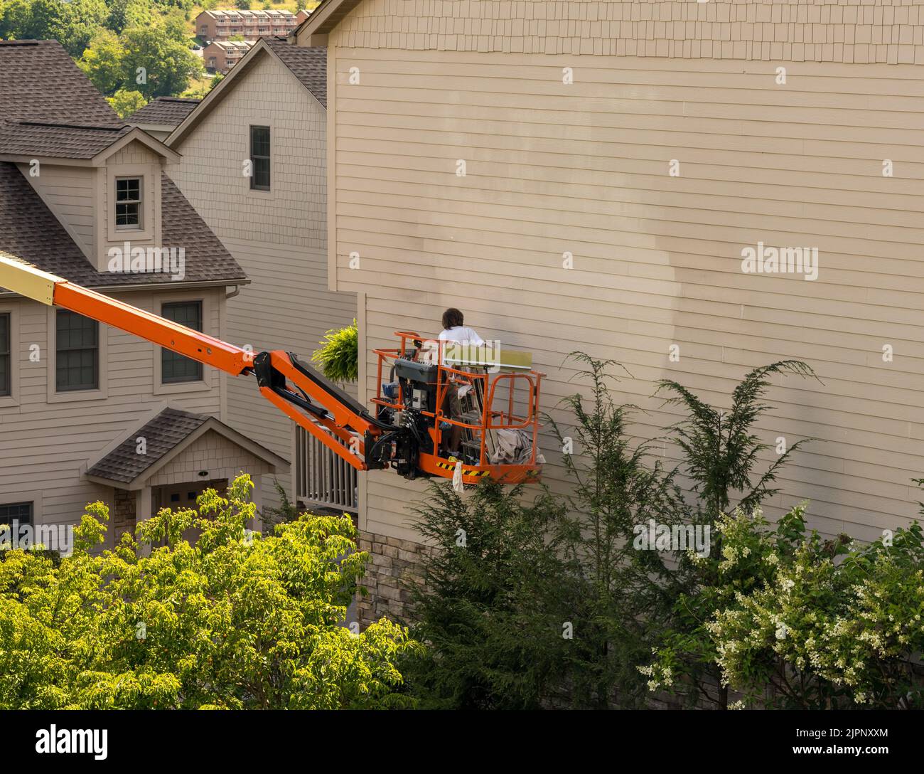Workman painting the side of a townhouse while standing in an articulating boom lift Stock Photo